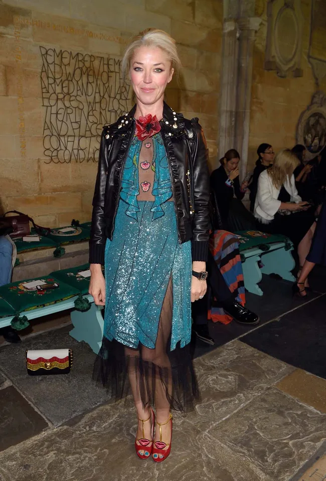 Person in a blue sequin dress with black leather jacket and red shoes at a fashion event.