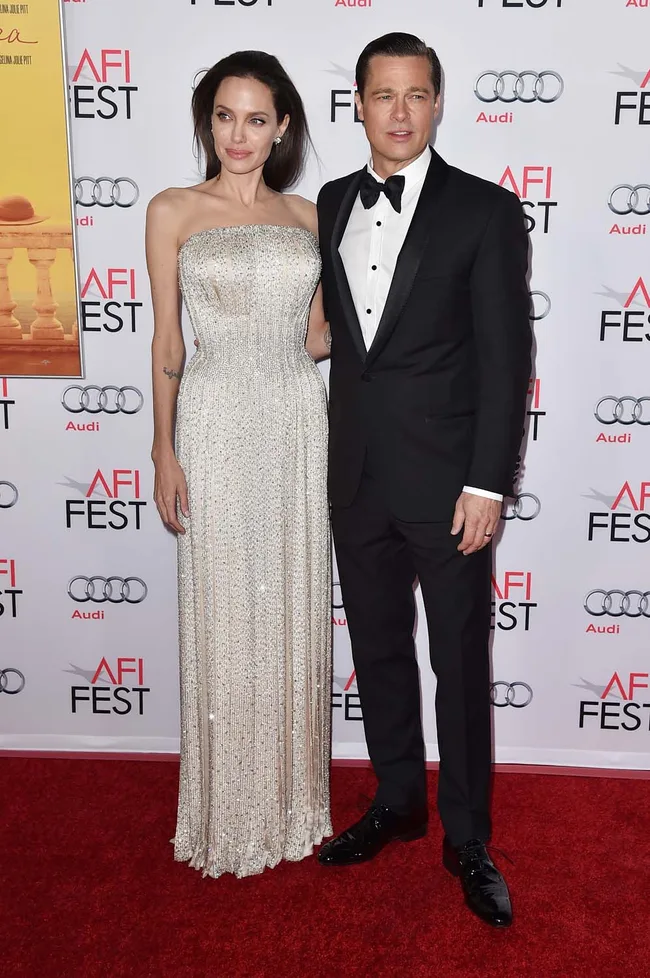 A man and woman pose on the red carpet at AFI Fest, she in a glittering gown, he in a black tuxedo.