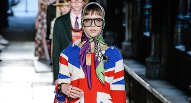 Model wearing British flag-inspired outfit and headscarf with large glasses on a runway.