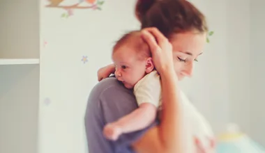 A woman holding a newborn baby on her shoulder in a softly lit room.
