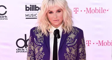 Singer at Billboard Music Awards in purple embellished suit and white blouse on red carpet, logo background.