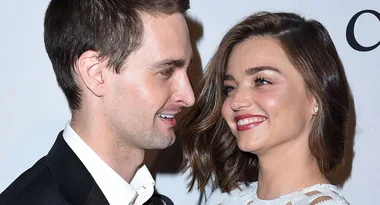 Two people smiling warmly at each other, one in a suit and the other in a white dress, at a formal event.