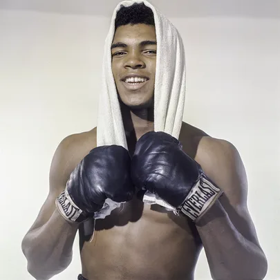 Young boxer with gloves and towel over head, smiling confidently.
