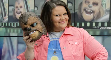 A woman smiling and holding a Chewbacca mask from Star Wars, with video stills in the background.