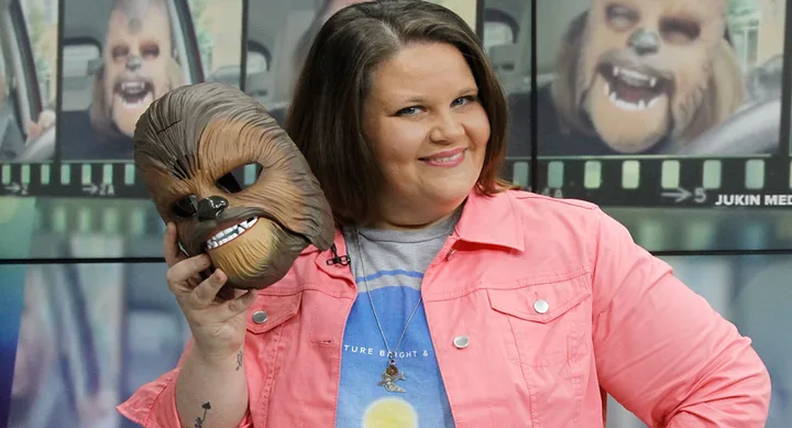 A woman smiling and holding a Chewbacca mask from Star Wars, with video stills in the background.