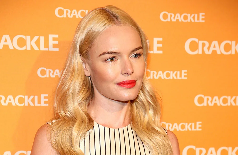 Blonde woman with red lipstick at a Crackle event, wearing a striped outfit. Orange Crackle logo background.
