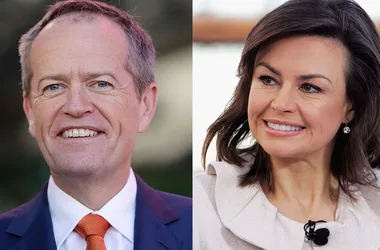 Two people smiling, one with short gray hair in a suit, the other with dark hair in an off-white outfit.