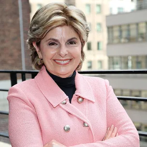 A person wearing a pink jacket and smiling, standing in front of an urban background.