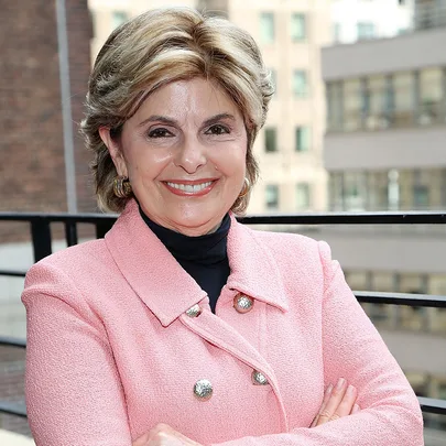 A person wearing a pink jacket and smiling, standing in front of an urban background.