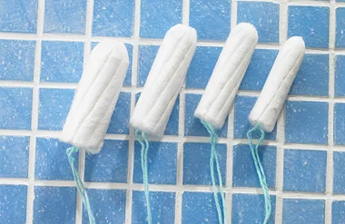Four white tampons with blue strings on a blue tiled surface.