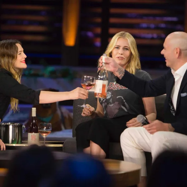 Three people sitting and sharing wine in a talk show setting.