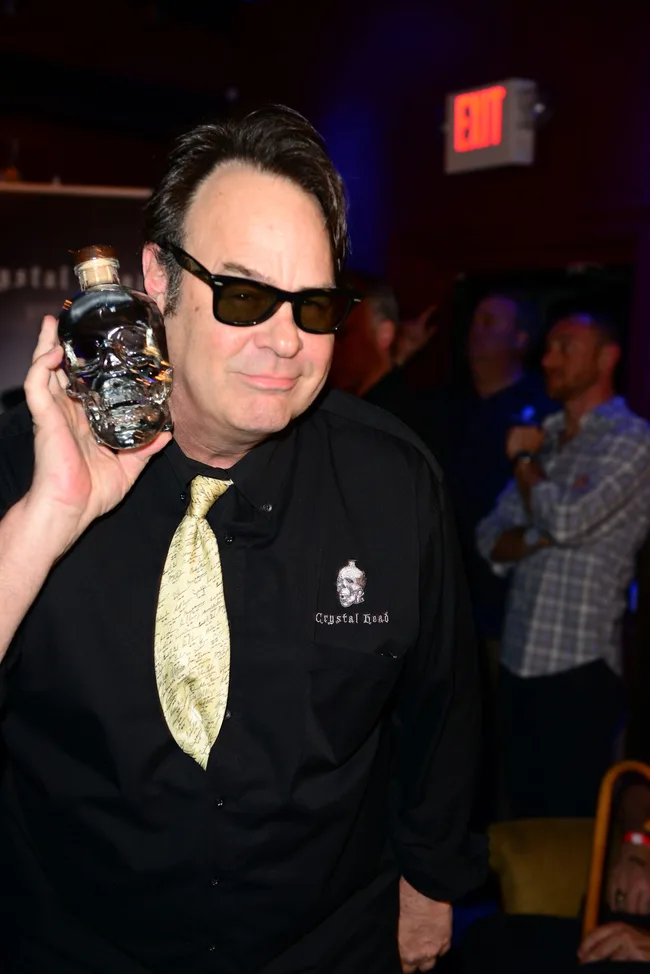 Man in sunglasses holding Crystal Head Vodka bottle beside face, wearing a black shirt with logo, at an indoor event.