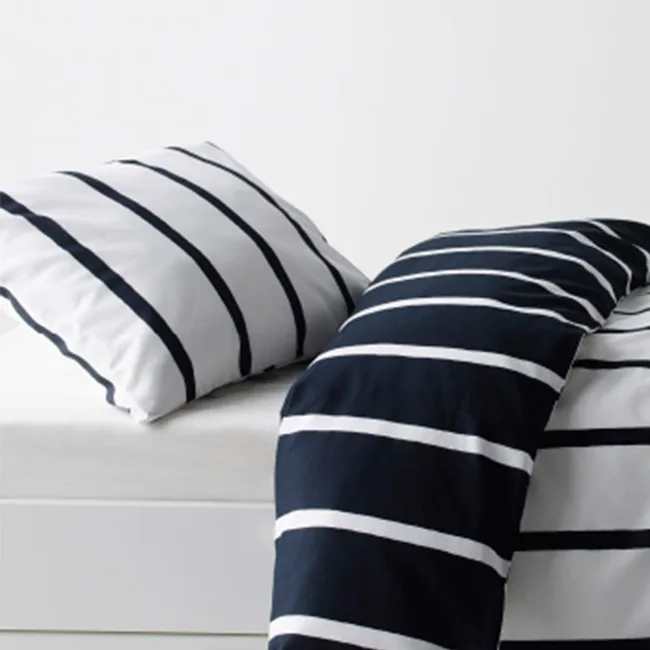 Striped black and white pillow and comforter on a white bed.