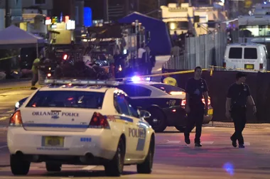 Police officers walking on a blocked-off street with police cars and emergency vehicles in Orlando at night.