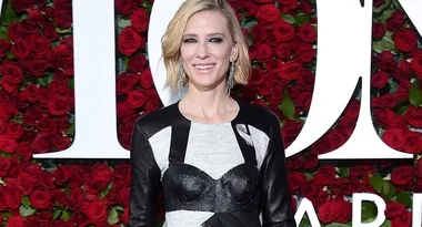 A person in a stylish black and white dress stands smiling against a backdrop of red roses.