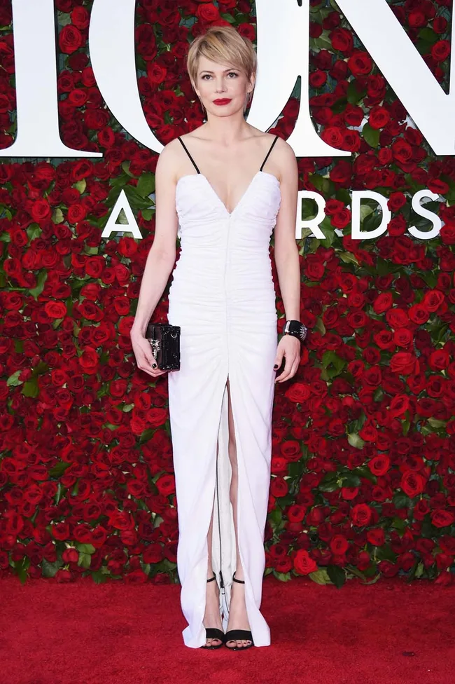 Woman in white dress on red carpet with red rose background at an awards event.