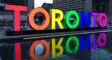 "Colorful 'Toronto' sign with rainbow reflection in a city plaza at dusk."