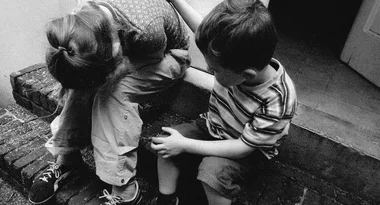 Children sitting on steps, one with head in hands, comforting each other. Black and white photo.
