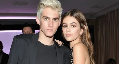 Young man with short blond hair and a young woman with long brown hair posing together indoors.
