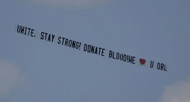Aerial banner reading "UNITE, STAY STRONG! DONATE BLOOD! WE ♥ U ORL" flying in the sky.