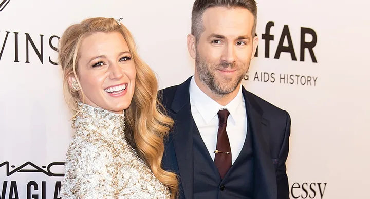A woman in a sparkling dress and a man in a suit smiling on a red carpet at an event.