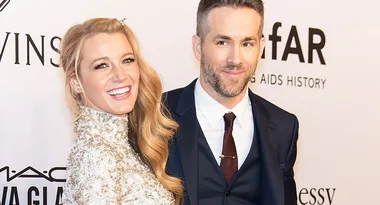 A woman in a sparkling dress and a man in a suit smiling on a red carpet at an event.