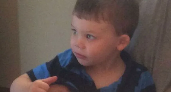 Toddler sitting on a couch, wearing a blue and black striped shirt, looking intently to the left.