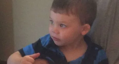Toddler sitting on a couch, wearing a blue and black striped shirt, looking intently to the left.