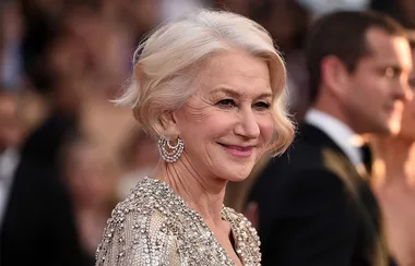 Elegant woman with short blonde hair smiling, wearing a sequin gown and ornate earrings on a formal occasion red carpet.