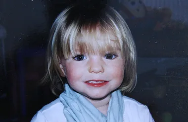A young child with blonde hair and a blue scarf smiles at the camera.