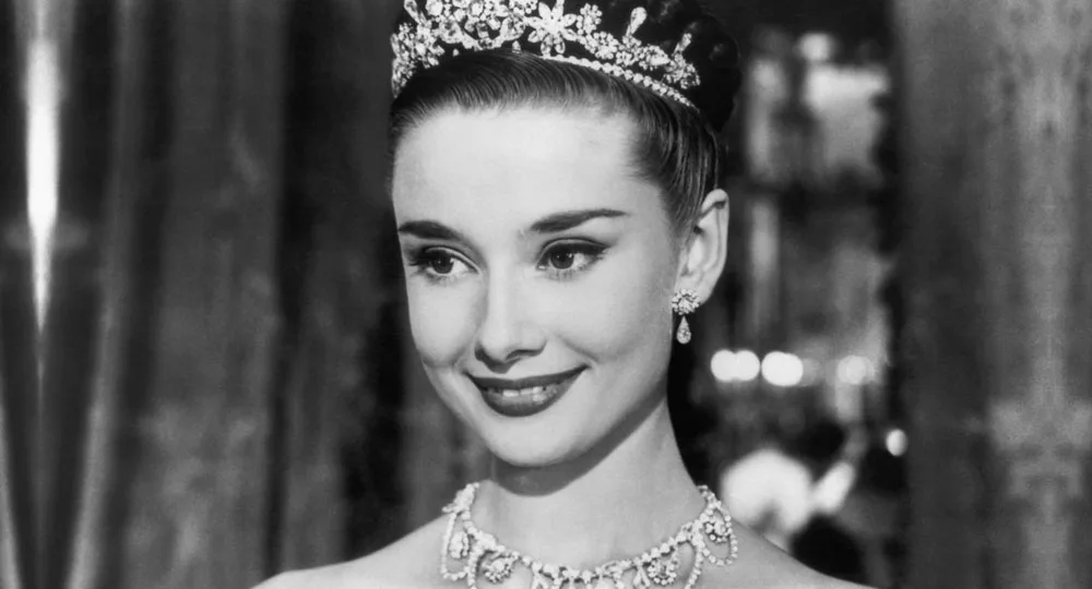 Black and white image of a woman smiling, wearing an ornate tiara and necklace.