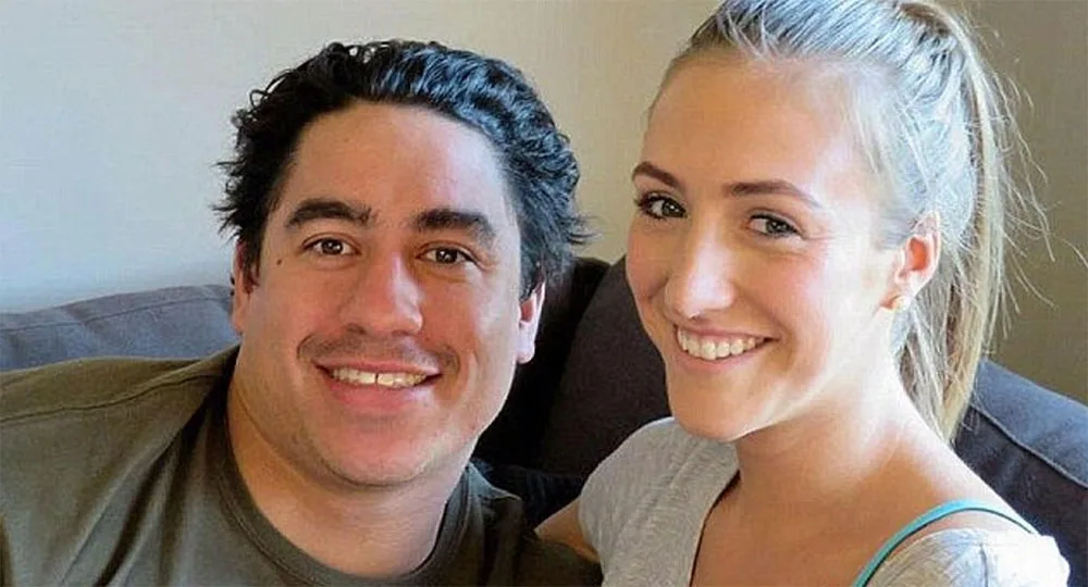 A smiling man and woman sitting on a couch, close together, in a casual setting.