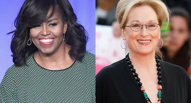 Two women smiling, both with medium-length hair; one in a patterned top, the other in a black outfit with a beaded necklace.