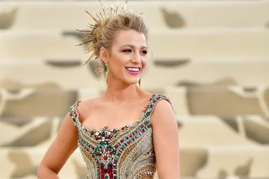 A person in an elegant, bejeweled dress with a gold spiked hair accessory, smiling at a formal event.