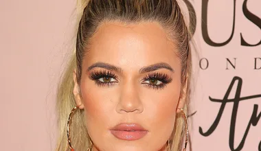 I don't know who this person is, but they have long lashes, hoop earrings, and a high ponytail against a pink background.