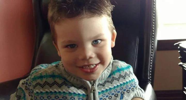 Young child smiling in a chair, wearing a patterned sweater.