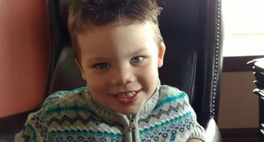 Young child smiling in a chair, wearing a patterned sweater.