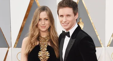 Couple posing on the red carpet at an awards ceremony, with elegant attire and geometric background.