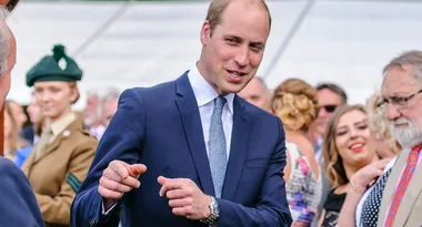 A man in a suit gestures while talking to others in a formal outdoor setting.