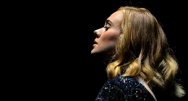 Profile of a woman with shoulder-length blond hair and a sparkly outfit against a dark background.