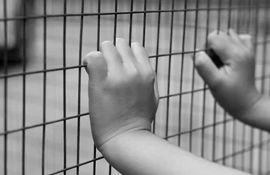 Child's hands gripping a wire fence, black and white photo.