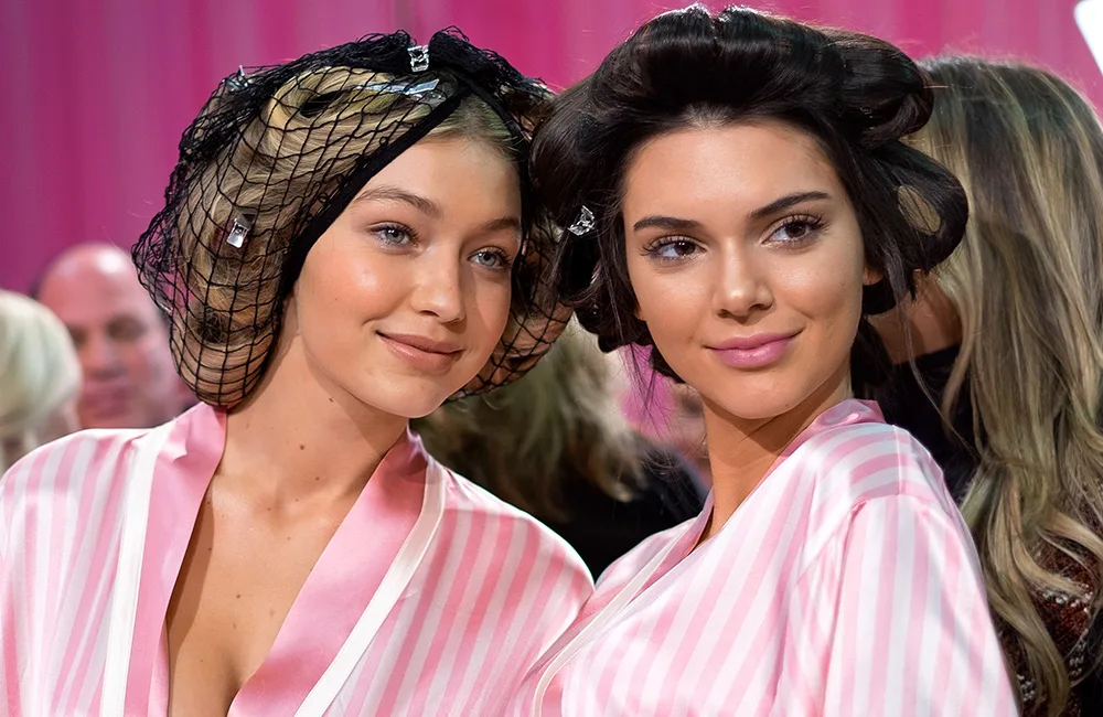 Models wearing pink striped robes with hair in curlers and nets backstage.