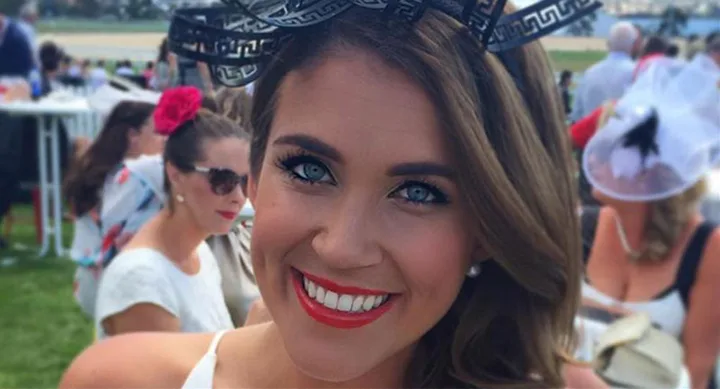 A woman with brown hair and a headpiece smiles at an outdoor event with people in the background.