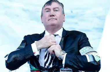 Man in a soaked suit adjusts tie with wet hair, wearing a wristwatch, sky in the background.