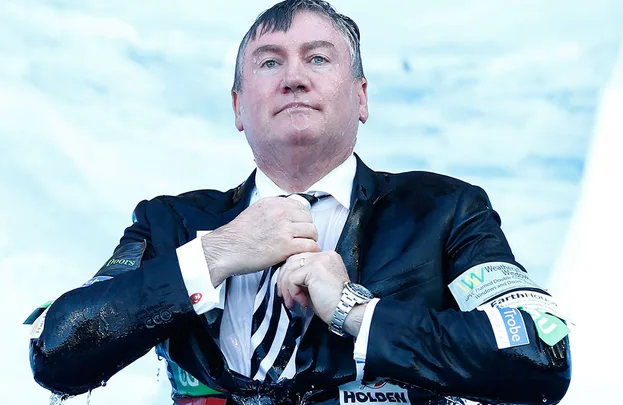 Man in a soaked suit adjusts tie with wet hair, wearing a wristwatch, sky in the background.