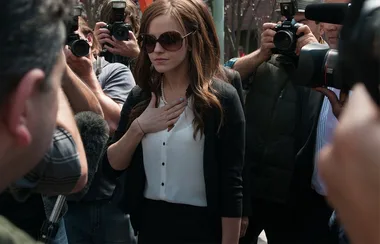 A woman in sunglasses surrounded by paparazzi photographers.