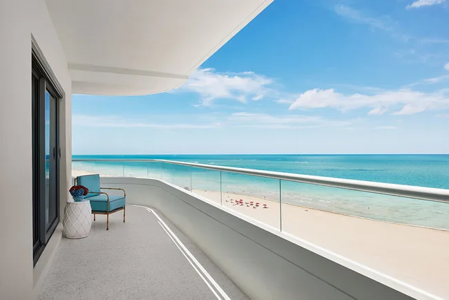 Balcony with blue chair overlooking beach and ocean, under clear blue sky.