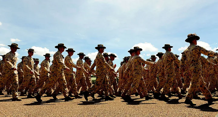 Australian soldiers in camouflage uniforms and hats marching in formation under a clear blue sky.