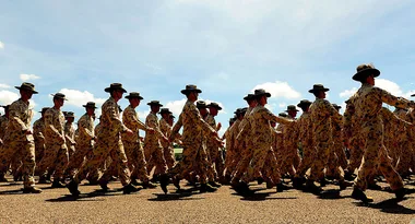 Australian soldiers in camouflage uniforms and hats marching in formation under a clear blue sky.