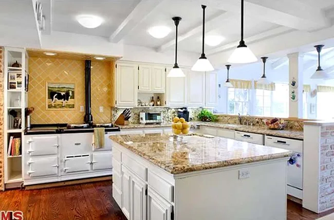 Bright kitchen with granite island, hanging lights, white cabinets, and a decorative backsplash above the stove.